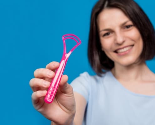 beautiful-happy-young-woman-with-tongue-scraper-blank-blue-background